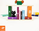 By the Book by FoxMind is a colorful mechanical puzzle featuring vibrant blocks resembling books in various colors. A playful black cat figure adds charm, while a flower-adorned planter sits on top, creating an engaging and whimsical display.