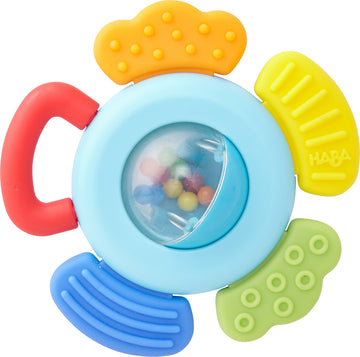 The Grasping Toy Blossom by Haba features a colorful design with a central transparent dome containing small, multicolored beads. It has four textured petals in red, yellow, green, and blue, providing tactile stimulation. The sturdy handle allows for easy gripping, making it ideal for infants to explore and enjoy sensory play.
