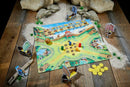A vibrant board game called 'Valley of the Vikings' by Haba. The game board features a colorful Viking village with area for placing tokens and small Viking ships. Pieces include a wooden ball, colorful player tokens in red, blue, green, and yellow, and Viking characters on boats. The setting is on a rustic wooden table with rocks and grass elements surrounding the game.