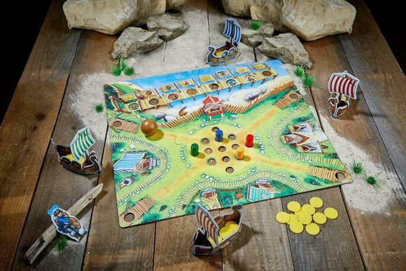 A vibrant board game called 'Valley of the Vikings' by Haba. The game board features a colorful Viking village with area for placing tokens and small Viking ships. Pieces include a wooden ball, colorful player tokens in red, blue, green, and yellow, and Viking characters on boats. The setting is on a rustic wooden table with rocks and grass elements surrounding the game.