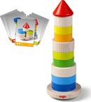 The Stacking Game Wobbly Tower by Haba features a colorful design with a tower made of wooden blocks in various colors—red, yellow, green, blue, and orange—stacked on a round base. Accompanying the tower are several task cards that challenge players to recreate specific arrangements, enhancing their dexterity and spatial awareness.