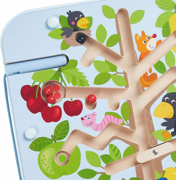 A colorful magnetic game board featuring a tree design with playful illustrations of animals like a bird, fox, and worm. The board includes bright red and green cherries and various leaves, with small magnetic balls positioned in different areas for gameplay. Made by Haba, this game encourages fine motor skills and interactive play for children.