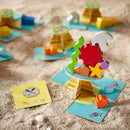 The Flotsam Float game by Haba features colorful wooden pieces shaped like sea creatures, coral, and islands. Players build and stack pieces on vibrant game boards, set against a sandy background. The game encourages creativity and fine motor skills as players strategize to keep their structures balanced while competing with others.