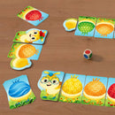 Colorful Rainbow Caterpillar game by HABA featuring vibrant cards with playful illustrations of a cheerful character and various patterned shapes. The game setup includes a wooden dice and several game pieces arranged on a wooden table, inviting fun for children.