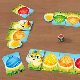 Colorful Rainbow Caterpillar game by HABA featuring vibrant cards with playful illustrations of a cheerful character and various patterned shapes. The game setup includes a wooden dice and several game pieces arranged on a wooden table, inviting fun for children.