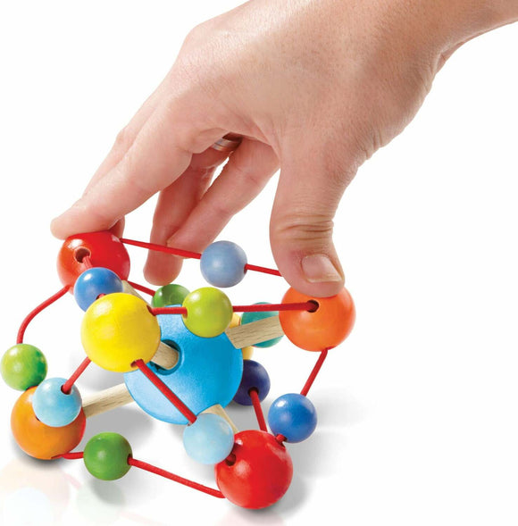 A colorful grasping toy named Tirili by Haba, featuring various-sized wooden and plastic balls connected by red elastic strings. A hand is seen grasping the toy, illustrating its interactive and engaging design for sensory play. The toy encourages fine motor skills and dexterity in young children.