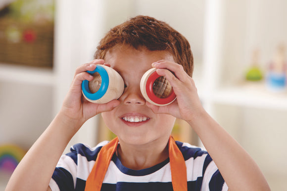 child holding two round wooden toys up to his eyes, the plastic lenses are faceted.