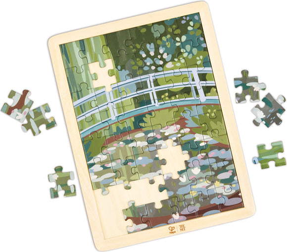 jigsaw puzzle in wooden frame depicting an illustrated bridge over a water-lily covered pond