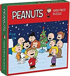 Peanuts Christmas jigsaw puzzle featuring 1000 pieces, showcasing beloved characters from the Peanuts comic strip celebrating around a Christmas tree in a wintery scene. The box displays cheerful characters such as Charlie Brown, Snoopy, and friends, creating a festive atmosphere perfect for holiday fun.