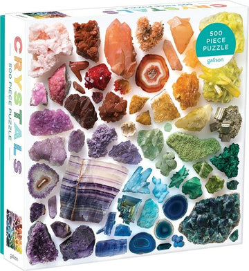 A 500-piece jigsaw puzzle titled 'Rainbow Crystals' by Galison. The puzzle features a vibrant collection of various crystal formations, showcasing intricate details and bright colors, including purple amethyst, deep blue lapis lazuli, and golden citrine. The design provides an engaging and colorful visual experience suitable for puzzle enthusiasts.