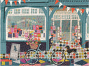 A vibrant jigsaw puzzle titled 'Book Haven' by Galison, depicting a charming bookstore exterior with colorful book displays, a bicycle adorned with flowers, and a playful dog. The scene showcases a lively atmosphere with a pattern of tiles on the ground, enhancing the whimsical feel of the puzzle.