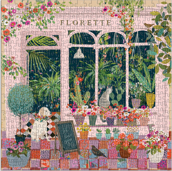 A colorful jigsaw puzzle featuring a charming indoor garden scene. The design includes vibrant flowers in pots, lush greenery, and playful cats, set against a pink window backdrop. A decorative chalkboard adds personalization to the cozy atmosphere.