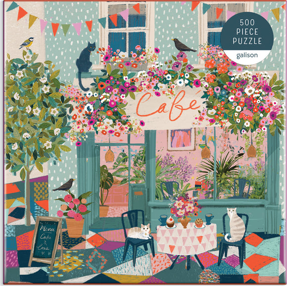 A colorful 500-piece jigsaw puzzle titled 'Afternoon Tea' by Galison. The illustration features a charming café scene adorned with vibrant flowers, playful cats, and decorative bunting. The café, highlighted by a sign reading 'Cafe,' displays a cozy outdoor setting with a round table set for tea, featuring cupcakes and a flower arrangement amidst a bright, patterned floor.