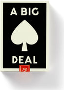 A Big Deal Giant Playing Cards by Chronicle Books displayed in a playful and bold design, featuring a prominent black background with white text and a central spade icon. Ideal for gatherings and game nights, these oversized cards promise fun and entertainment.