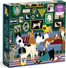 The Lounge Dogs Foil jigsaw puzzle by Galison features an illustration of various dog breeds lounging on a couch, surrounded by framed dog-themed art. The scene is colorful and playful, showcasing a cozy home environment with several playful puppies and dogs, including a corgi, a bulldog, and a beagle. The puzzle contains 500 pieces, making it suitable for both children and adults who enjoy assembling jigsaw puzzles.