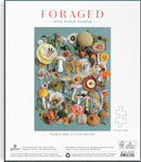 Galison Foraged 1000 Piece Jigsaw Puzzle featuring a vibrant assortment of mushrooms and botanical elements arranged artfully against a teal background. The puzzle size is 27 x 20 inches, providing a challenging and visually appealing experience for puzzle enthusiasts.