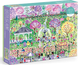 A colorful jigsaw puzzle box titled 'Easter Egg Hunt' by Michael Storrings, manufactured by Galison. The illustration depicts a vibrant park scene filled with people, bunnies, and blooming trees amidst a festive Easter egg hunt. The puzzle consists of 1000 pieces and showcases various activities such as children searching for eggs and enjoying the festivities.