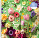 Galison's 'Springtime Petals' jigsaw puzzle featuring an intricate arrangement of various colorful flowers including tulips, ranunculus, daffodils, and pansies set against a vibrant green background. The puzzle consists of 500 pieces, inviting floral enthusiasts to enjoy a delightful and challenging activity.