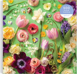 Galison's 'Springtime Petals' jigsaw puzzle featuring an intricate arrangement of various colorful flowers including tulips, ranunculus, daffodils, and pansies set against a vibrant green background. The puzzle consists of 500 pieces, inviting floral enthusiasts to enjoy a delightful and challenging activity.