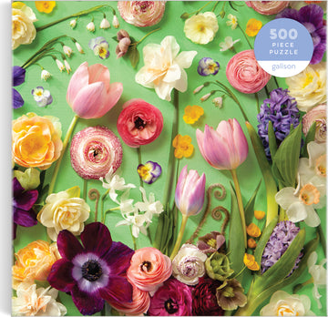 Galison's 'Springtime Petals' jigsaw puzzle featuring an intricate arrangement of various colorful flowers including tulips, ranunculus, daffodils, and pansies set against a vibrant green background. The puzzle consists of 500 pieces, inviting floral enthusiasts to enjoy a delightful and challenging activity.