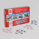 LEGO Puzzle Christmas Train jigsaw puzzle featuring four connecting 100-piece puzzles. The box displays festive scenes with a train, snow, and holiday characters. Several puzzle pieces scattered around the box, showcasing colorful designs.