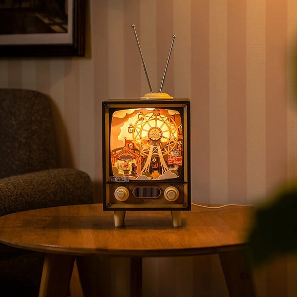 The Music Dreamer Sunset Carnival DIY kit by Robotime features a vintage-style TV lamp with decorative carnival scenes illuminated inside. The warm light highlights attractions such as a ferris wheel and colorful carnival booths, creating a whimsical atmosphere. The setup includes detailed cutouts and a charming design, ideal for adding a unique touch to any home decor.