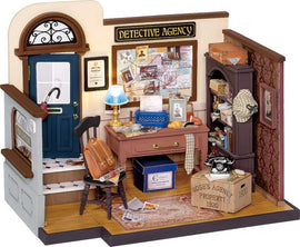 A detailed model of Mose's Detective Agency interior, featuring a blue door, a wooden desk with a typewriter and various papers, a chair with a brown backpack, a lamp, and a phone on a box labeled 'Mose's Agency.' The walls display a bulletin board covered with case files and photos, and a bookshelf filled with assorted items.