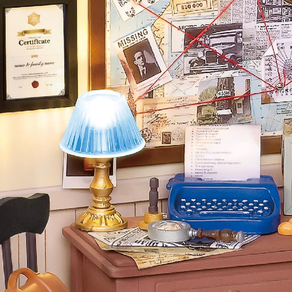 A cozy detective agency setup featuring a lamp with a blue shade, a vintage blue typewriter, a magnifying glass, and various documents. The wall is decorated with a map and notes connected by red string, creating a mysterious ambiance.