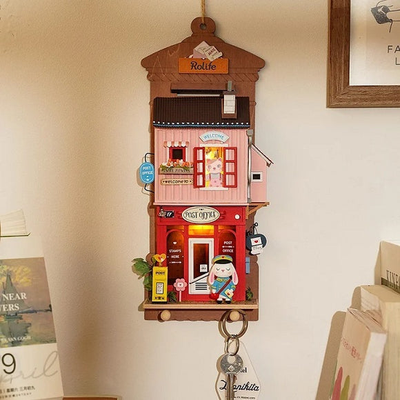 The Love Post Office DIY kit by Robotime features an intricately designed miniature post office. It showcases vibrant colors with details like a red postal office, a welcoming sign, various postal items, and a charming character. Perfect for crafting enthusiasts, this kit adds a decorative touch to any space.