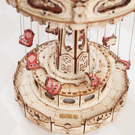 A detailed view of the Swing Ride DIY Model by Robotime, featuring multiple intricately designed swing seats hanging from a circular structure. The model showcases elaborate engravings and a wooden finish, emphasizing its craftsmanship and inviting users to engage in a fun, creative assembly experience.