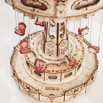 A detailed view of the Swing Ride DIY Model by Robotime, featuring multiple intricately designed swing seats hanging from a circular structure. The model showcases elaborate engravings and a wooden finish, emphasizing its craftsmanship and inviting users to engage in a fun, creative assembly experience.