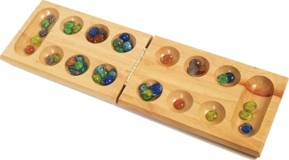 A wooden Mancala game board displayed open, featuring two rows of shallow pits filled with colorful glass marbles. The board is crafted from smooth wood with a hinge in the center for easy storage. The marbles are in various shades of green, blue, and orange, enhancing the visual appeal of this classic strategy game.