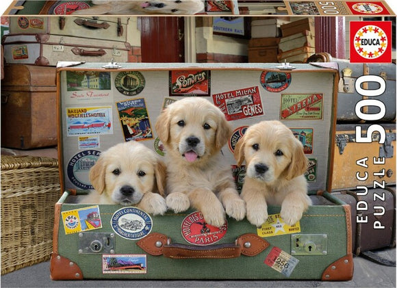 A charming jigsaw puzzle titled 'Puppies in the Luggage' by Educa featuring three adorable golden retriever puppies playfully positioned inside a vintage suitcase covered in travel stickers and labels. The scene is warm and inviting, evoking a sense of adventure and cuteness.