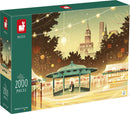 The New York Bustle jigsaw puzzle by Juratoys features a festive winter scene with a gazebo and iconic skyscrapers in the background. The puzzle box displays vibrant artwork depicting holiday lights and decorations. It contains 2000 pieces and is made in Europe, perfect for puzzle enthusiasts looking for a challenging and beautiful design.