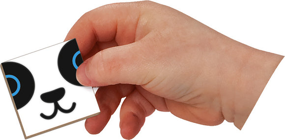 A child's hand holding a magnetic square piece featuring a panda face design with large eyes and a smiling mouth, part of the Mix & Match Magneti' Book by Juratoys. This interactive toy encourages creativity and imaginative play.