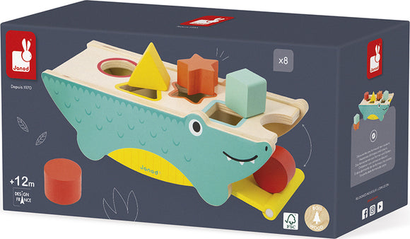 The Tropik Shape Sorting Crocodile by Janod is a playful wooden toy designed for children aged 12 months and up. It features a crocodile-shaped base with cut-outs to fit various geometric shapes including a star, triangle, and circle. The crocodile is adorned with a cheerful face and vibrant colors, encouraging early learning through shape recognition and motor skills development. The included shapes come in different colors and forms, making it a delightful addition to any child's playtime.