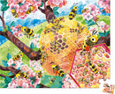 A colorful jigsaw puzzle featuring a busy bee scene with blooming pink flowers and a honeycomb hive. Numerous cartoon-style bees fly around, showcasing a vibrant countryside setting with greenery and a bright blue sky.