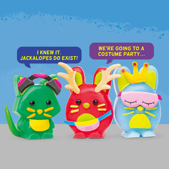 Three colorful wax animal figures: a green cat with pink headphones, a red rabbit with antlers, and a blue bunny wearing a crown and a mask. They are posed with playful expressions and speech bubbles saying humorous phrases.