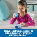 A young girl in a pink long-sleeve shirt is sitting at a table, engaging with the Cool Down Cubes Sensory Fidget game from Learning Resources. She is smiling while holding a blue cube and interacting with the game, which includes colorful sensory elements designed for calming activities. The background is soft and inviting, enhancing the focus on her playful and focused expression.