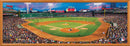 A vibrant panoramic jigsaw puzzle featuring Fenway Park, home of the Boston Red Sox, bustling with fans in the stands. The scene captures a game in progress with players on the field, green grass, and the famous Green Monster scoreboard in the background, framed in a wooden border.