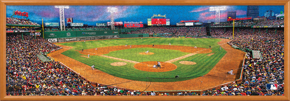 A vibrant panoramic jigsaw puzzle featuring Fenway Park, home of the Boston Red Sox, bustling with fans in the stands. The scene captures a game in progress with players on the field, green grass, and the famous Green Monster scoreboard in the background, framed in a wooden border.