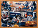 A vibrant jigsaw puzzle featuring a festive New England Patriots gameday scene. The image showcases a pickup truck adorned with Patriots gear, including jerseys and flags. Cheerful fans wearing helmets and jerseys are enjoying tailgate food like burgers, while accessories like coolers and footballs enhance the gameday atmosphere.