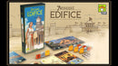 7 Wonders: Edifice board game by Asmodee featuring colorful game components, including cards, buildings, and tokens. The box art depicts a woman holding a scroll, standing next to a historical structure. The background highlights architectural designs and illustrations related to the game theme.