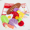 Colorful felt pieces representing various sandwich ingredients, including lettuce, tomato, cheese, bacon, and a fried egg, accompanied by a guest check order pad and a matching game card. The vibrant elements encourage creative play and learning about food.