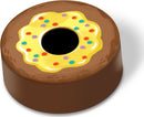 A colorful game piece shaped like a donut, featuring a yellow frosting top adorned with rainbow sprinkles, set against a brown base. This whimsical design is part of the BUSY BUSY BAKE SHOP game by Peaceable Kingdom, perfect for engaging creative playtime experiences.