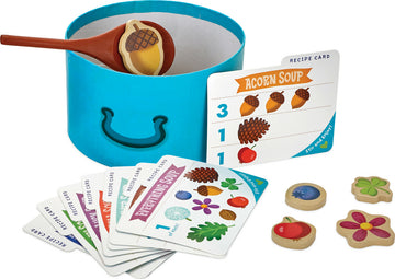 Acorn Soup game by Peacable Kingdom featuring a vibrant blue pot, wooden spoon, and various colorful recipe cards. The game includes charming food tokens like acorns, flowers, and fruits for engaging gameplay. Ideal for interactive playtime, encouraging creativity and social skills.