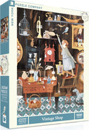 A vintage-themed jigsaw puzzle titled 'Vintage Shop' by New York Puzzle Company, showcasing a cozy antique shop filled with various nostalgic items including a clock, a birdcage, a sewing machine, and more. The scene features a character reaching for a decorative item while several other antiques are displayed around the shop, implying a whimsical atmosphere perfect for puzzle enthusiasts.