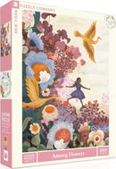 A beautifully illustrated jigsaw puzzle titled 'Among Flowers' by New York Puzzle Company. The puzzle features vibrant floral designs and a whimsical scene of a girl dancing in a field of flowers, surrounded by colorful blossoms and a flying bird. It includes 500 pieces and measures 24 x 18 inches when completed.