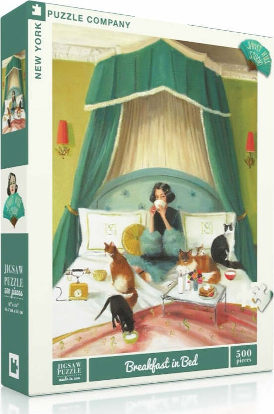 A colorful jigsaw puzzle box featuring a cozy scene of a woman enjoying breakfast in bed surrounded by playful cats. The artwork, by Janet Hill Studio, shows a bright green and pastel bedroom setting with pillows and a bed canopy. The scene includes various breakfast items and a charming atmosphere, perfect for puzzle enthusiasts.