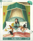 A colorful jigsaw puzzle featuring a serene breakfast scene in bed. A woman sips tea surrounded by five cats, with a cozy green canopy above and a flower vase on the tray beside a well-set breakfast.